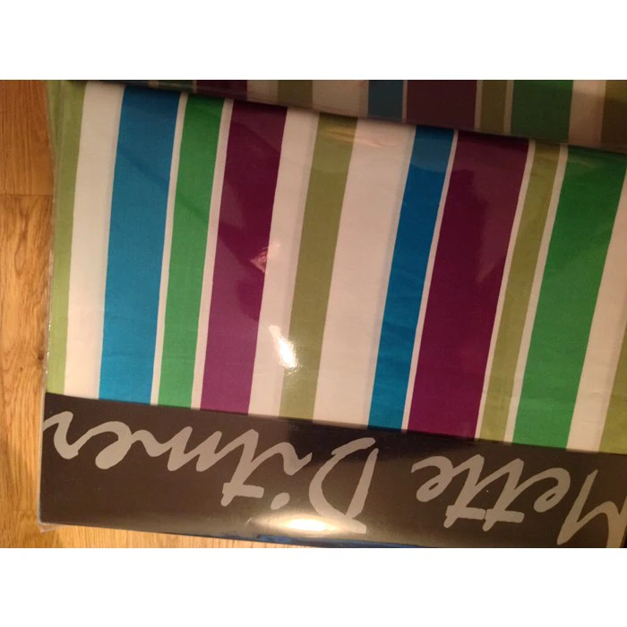 Et foldet stof med lodrette striber i blå, grøn, hvid og lilla, delvist indpakket i emballage med skrifttekst.